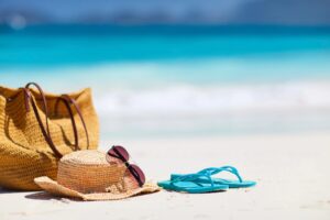 Beach bag, sun hat, and flip-flops on the sand by the ocean
