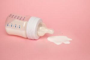 Tipped-over baby bottle with formula spilling out on a pink background