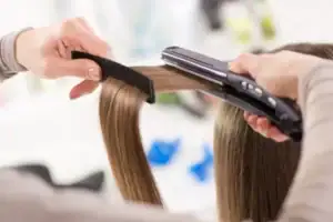 Woman seated in a salon having her hair straightened with a flat iron by a stylist
