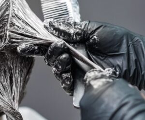 Gloved hands applying chemical relaxer to sections of dark hair